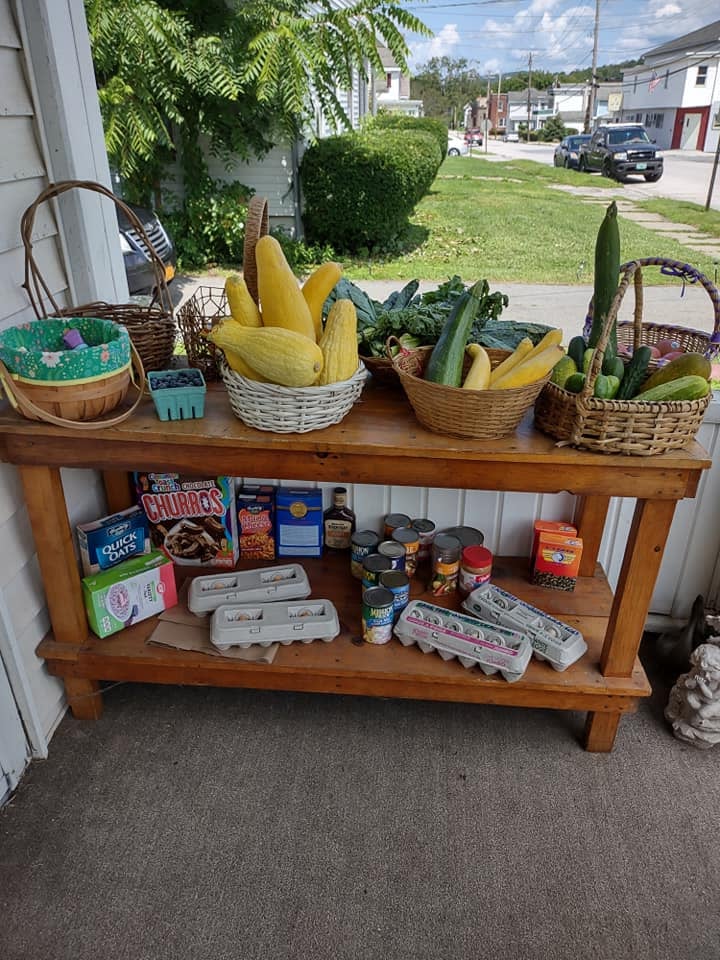 The Community Porch table on First St in Hoosick Falls, NY laid out with fresh produce, eggs, and donations, with the neighborhood behind