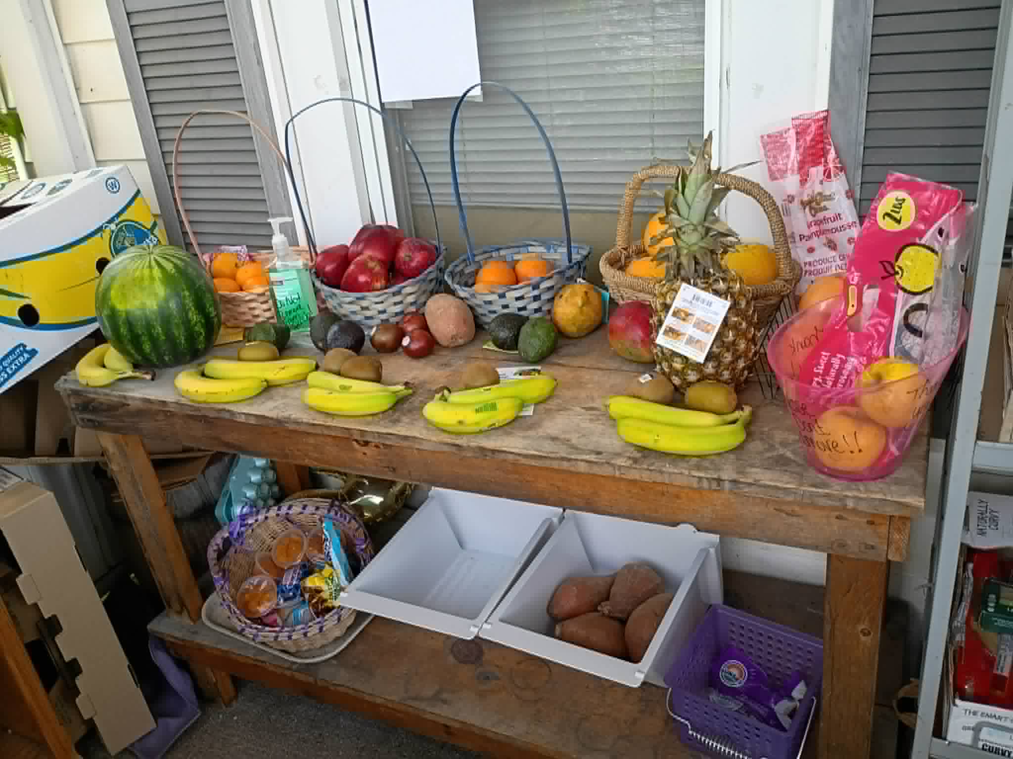 A porch table of fresh fruit including watermelon, bananas, pineapple, and apples at the Community Porch in Hoosick Falls NY
