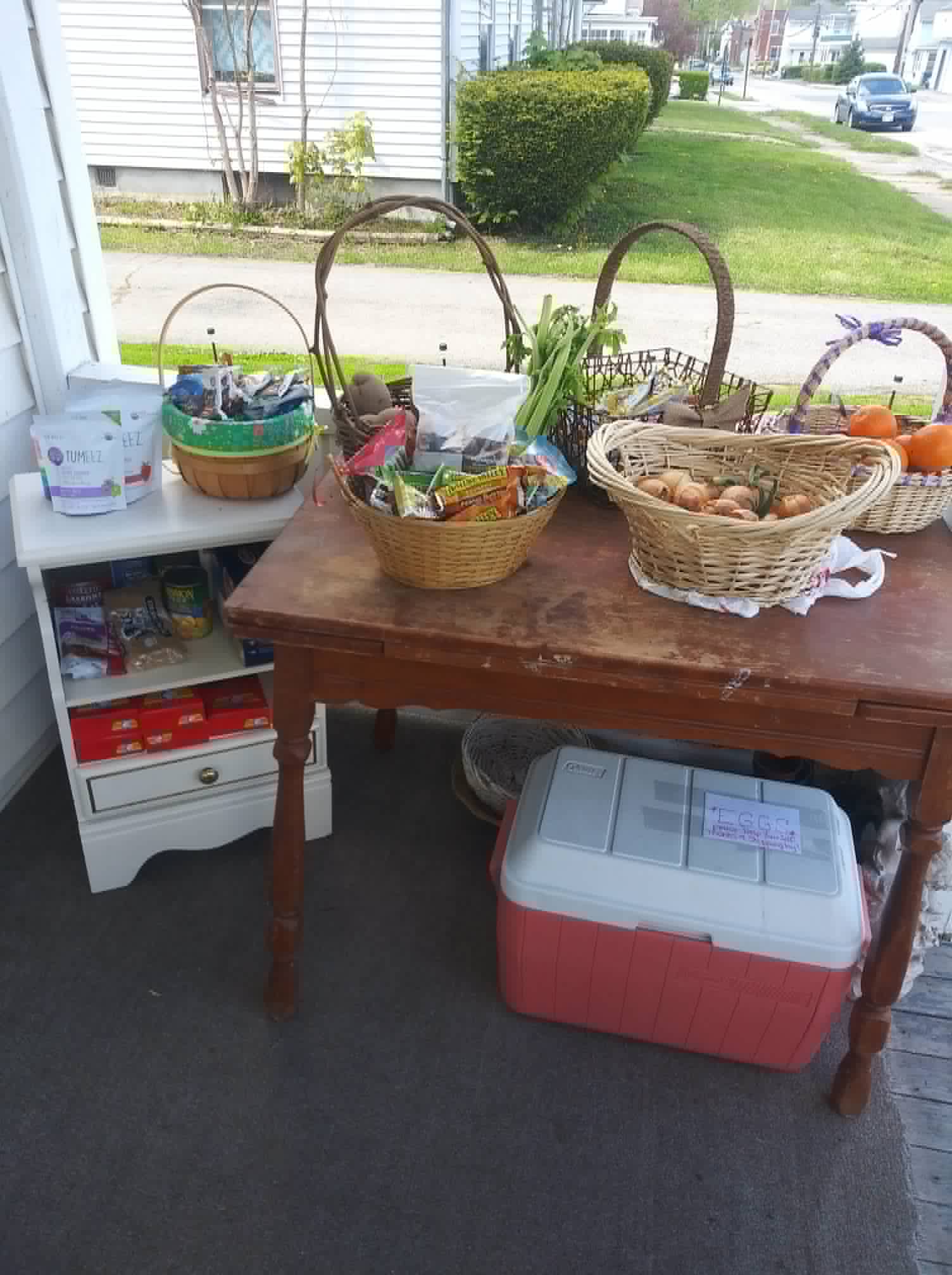 Baskets of onions, celery, and oranges on the Community Porch in Hoosick Falls NY with the neighborhood street behind